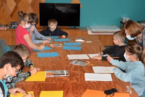 Dzieci siedząc przy dużym stole rysują na kolorowym kartonie