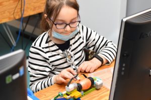 Uczestniczka zajęć siedząc przy stanowisku komputerowym, maluje pisankę dzięki skonstruowanemu przez siebie robotowi z klocków LEGO