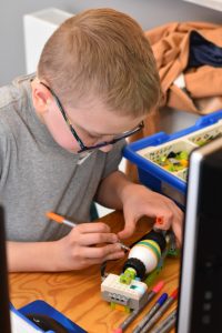 Uczestnik zajęć siedząc przy stanowisku komputerowym, maluje pisankę dzięki skonstruowanemu przez siebie robotowi z klocków LEGO