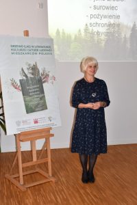 Hanna Czelej, Dyrektor GBP w Wyrykach stoi przy plakacie projektu, w tle na ścianie wyświetlona jest prezentacja