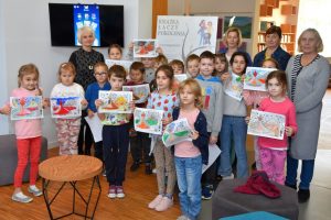 W przestrzeni biblioteki dzieci, nauczyciele oraz Hanna Czelej Dyrektor GBP Wyryki pozują do zdjęcia, dzieci trzymają w dłoniach swoje kolorowanki, w tle plakat wydarzenia