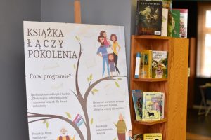 Po lewej plakat projektu na sztaludze, po prawej pułki biblioteczne a na nich wystawa ulubionych książek naszych dziadków, rodziców i dzieci