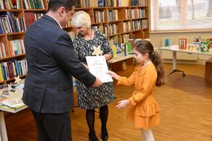 W przestrzeni biblioteki laureatka konkursu odbiera z rąk Wójta Gminy Wyryki nagrodę oraz dyplom, w tle półki pełne książek