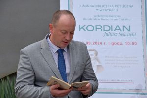 Bernard Błaszczuk – Wójt Gminy Wyryki podczas interpretacji wybranego utworu, w tle plakat wydarzeni oraz budynek GBP Wyryki