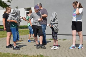 Grupa dzieci stojących na chodniku obok budynku biblioteki. Wszyscy biorą udział w grze.