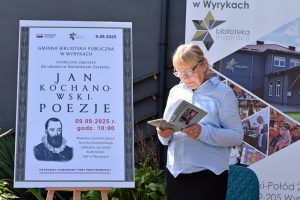 Kobieta czyta książkę obok plakatu Narodowego Czytania poezji Jana Kochanowskiego