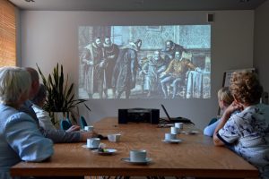 Grupa osób siedzi przy stole i ogląda projekcję filmu o życiu i twórczości Kochanowskiego