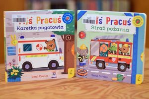 Dwie kolorowe książeczki dla dzieci z serii Miś Pracuś autorstwa Benjiego Daviesa stojące na drewnianym blacie.